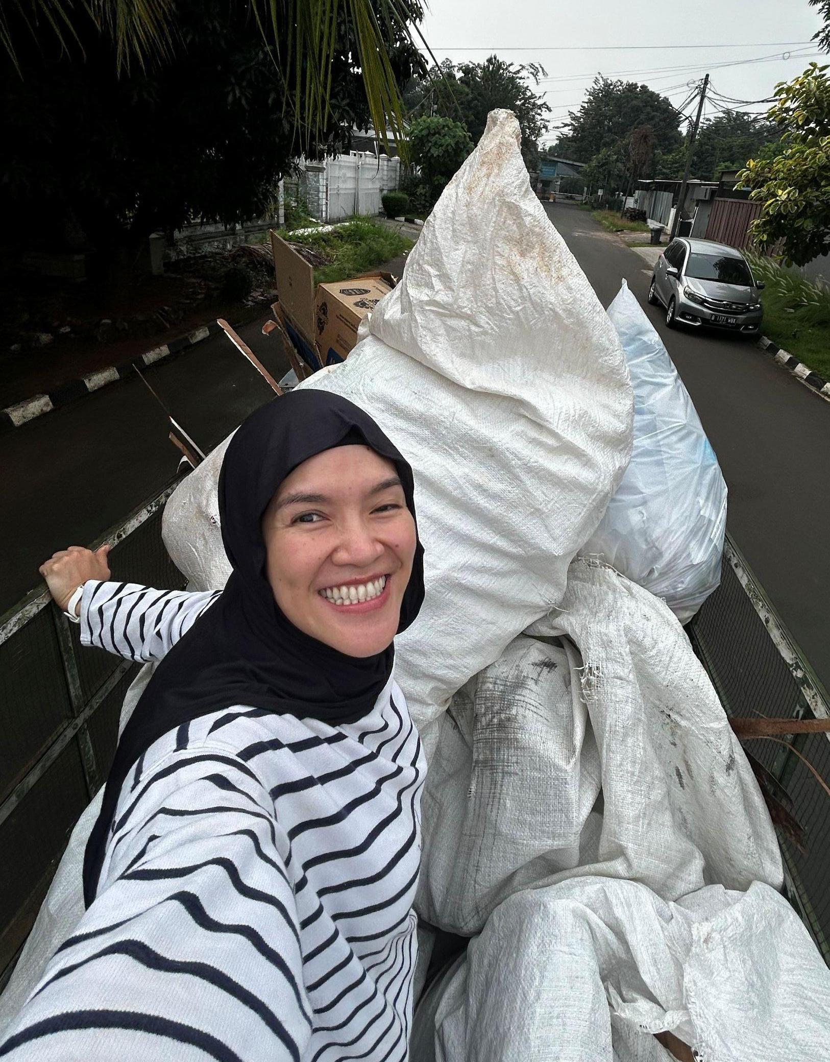 Nena, a smiling Indonesian women in a hijab, standing atop a truck with bags of sorted waste