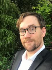 Photo of John Pearce, white male, in a suit, in front of greenery