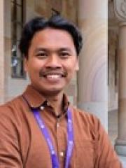 A headshot of Juddi – a smiling Javanese Indonesian man with short, dark-black, wavy hair standing at UQ's Great Court