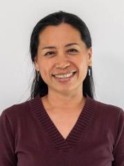 A headshot of Kabzeel Sheba Catapang - a brown woman with black waist-length hair wearing a maroon V-neck shirt and dangling earrings