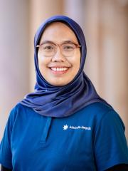 A headshot of Lisa – a women with hijab and glasses in front of the university building