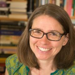 A photo of Jodie - a smiling white woman with glasses and shoulder-length brown hair