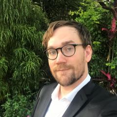 Photo of John Pearce, white male, in a suit, in front of greenery