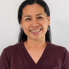A headshot of Kabzeel Sheba Catapang - a brown woman with black waist-length hair wearing a maroon V-neck shirt and dangling earrings